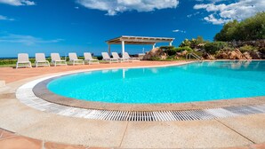 Una piscina azul cristalina con sillas de descanso y una pérgola, rodeada de formaciones rocosas naturales y follaje.