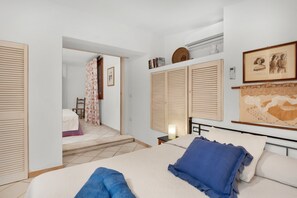 A bedroom with a bed, a nightstand, a wall-mounted air conditioner, and a door leading to another room.