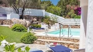 A pool area with lounge chairs, a stone wall, and a white fence. - Villa Ginepro with Private Pool, Sea View, 2 Terraces, Wi-Fi & Air Conditioning (San Teodoro)