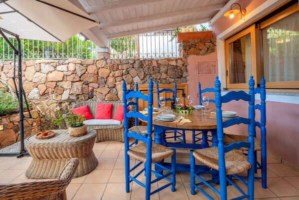 Een terras met een stenen muur, rieten meubels en blauwe stoelen.