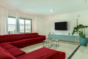 Una sala de estar moderna con un sofá seccional rojo, un televisor de pantalla plana montado en la pared, una planta grande en maceta y un mueble de color azul claro.