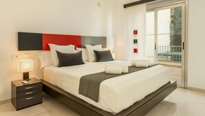 A modern hotel room with a large bed, a nightstand, a lamp, and a view of the outside. - Apartment "Happy Dreamer" with Large Pool, Mountain Views & Wi-Fi (Puerto Rico)