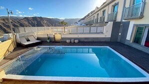A rooftop pool with a clear view of the mountains, a covered seating area, and a building with balconies. - Apartment "Happy Dreamer" with Large Pool, Mountain Views & Wi-Fi (Puerto Rico)