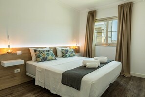A neatly made bed with pillows, a bedside table with a lamp, and a window with curtains. - Apartment "Happy Dreamer" with Shared Pool, Terrace and Mountain Views (Puerto Rico)