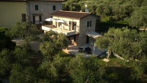 Une maison en pierre à deux étages, dotée d’un balcon, entourée de verdure et située dans un paysage vallonné.