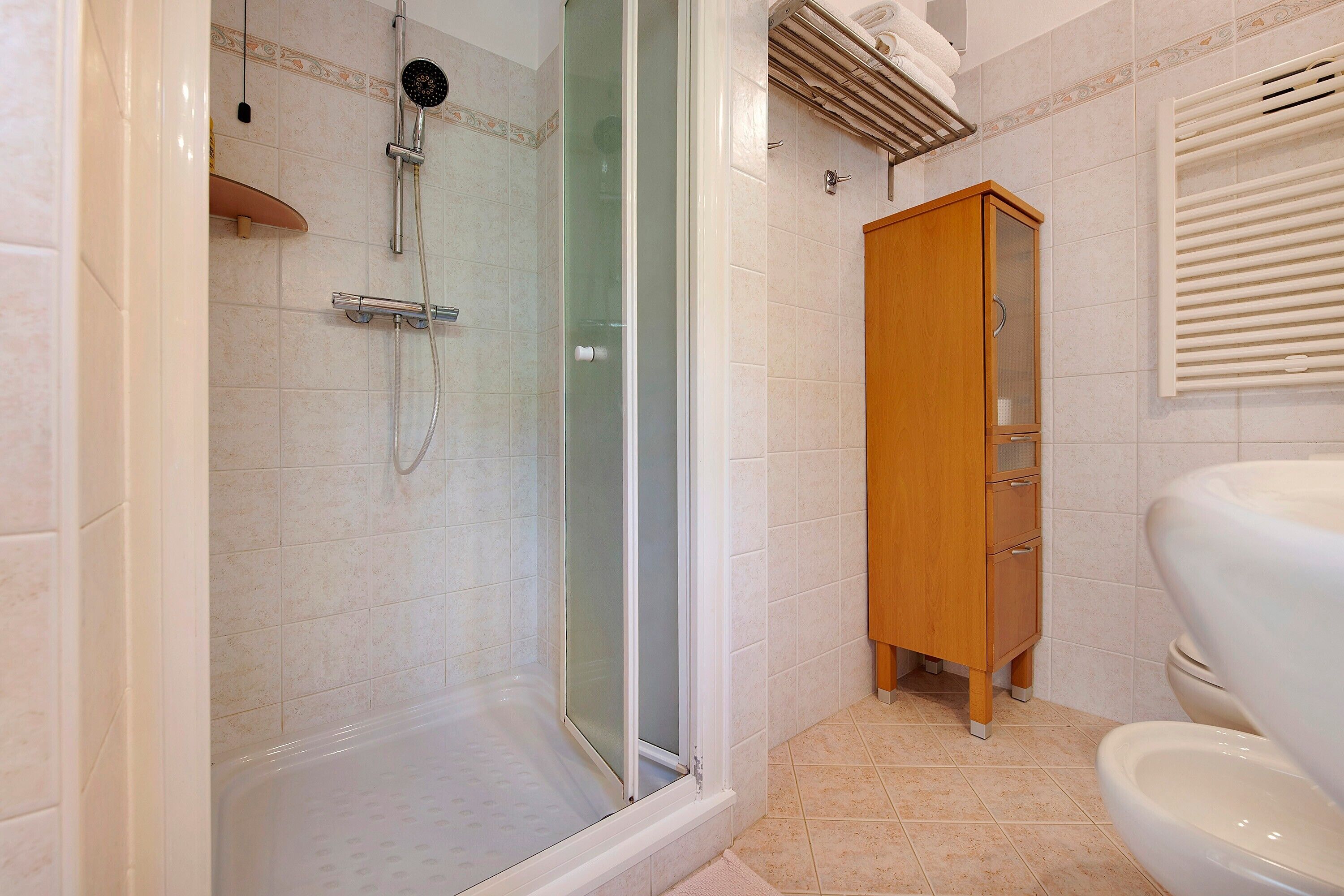 Ein Badezimmer mit Duschkabine aus Glas, einem Holzschrank und einer Toilette.