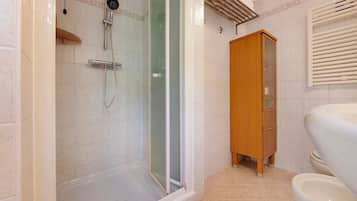 Ein Badezimmer mit Duschkabine aus Glas, einem Holzschrank und einer Toilette.