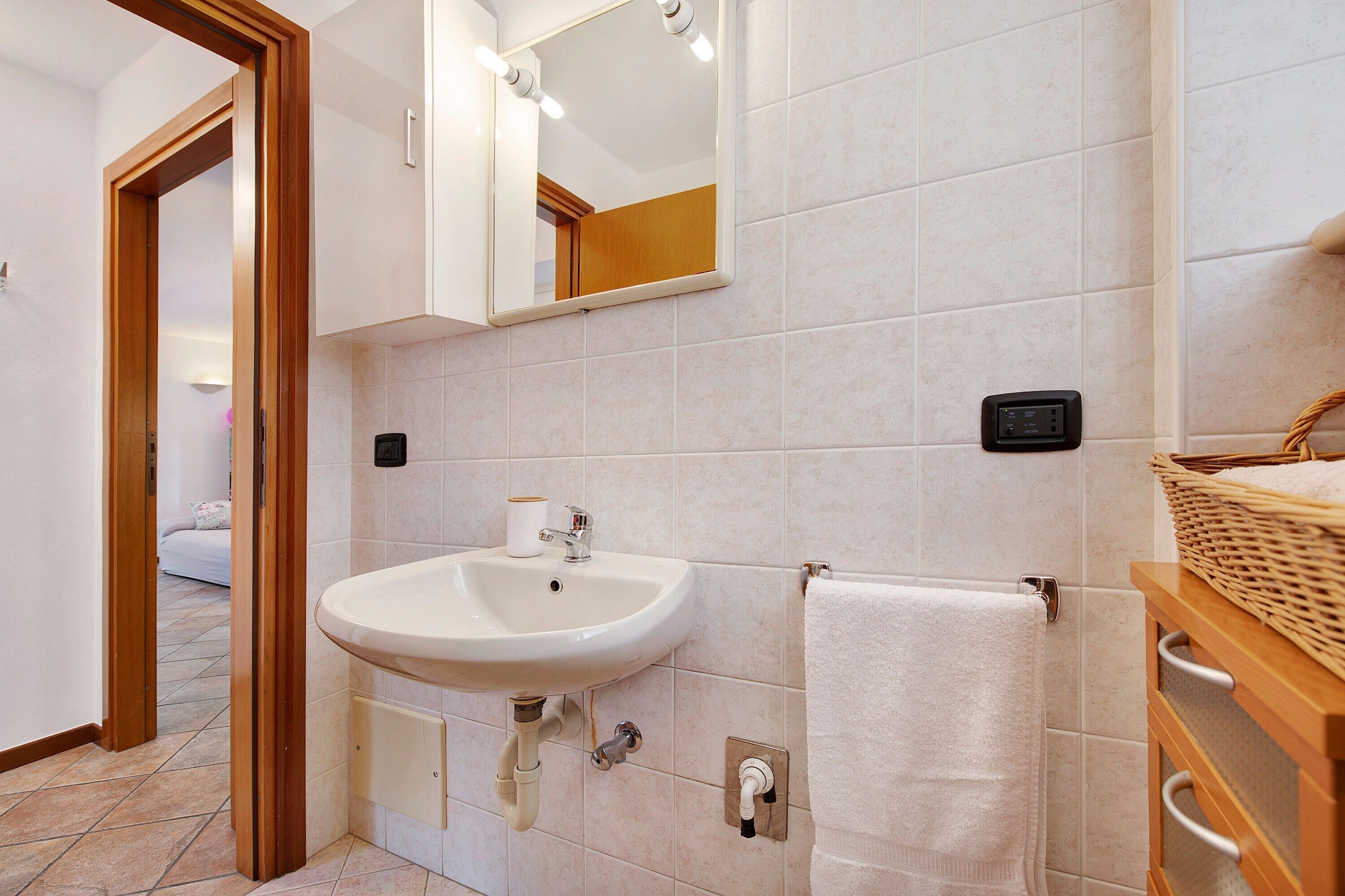 A bathroom with a sink, mirror, towel rack, and a wall-mounted control panel.