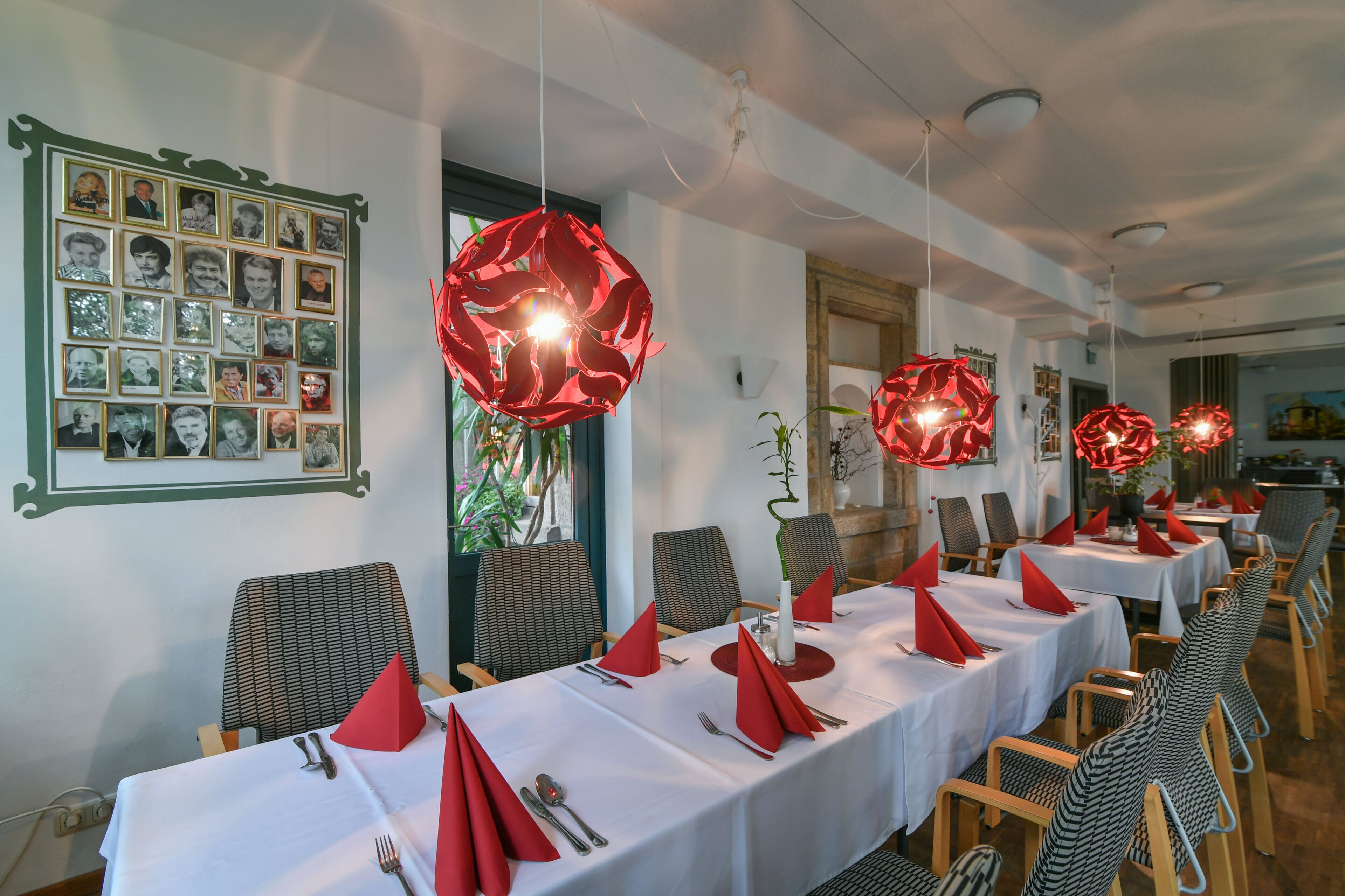 Een restaurant met lange tafels gedekt voor het diner, rode servetten en een wand vol ingekaderde foto's.