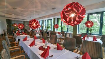 A dining area with tables set for multiple guests, featuring red napkins and a modern chandelier.