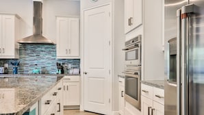Une cuisine moderne avec des meubles blancs, des appareils en acier inoxydable et un dosseret de carrelage bleu.