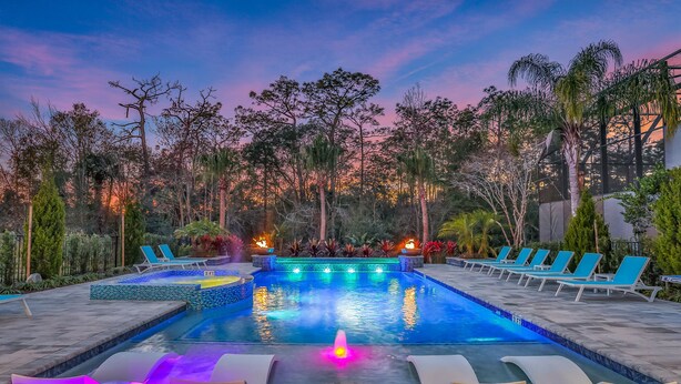 A swimming pool with lounge chairs and a fountain, surrounded by trees and plants.