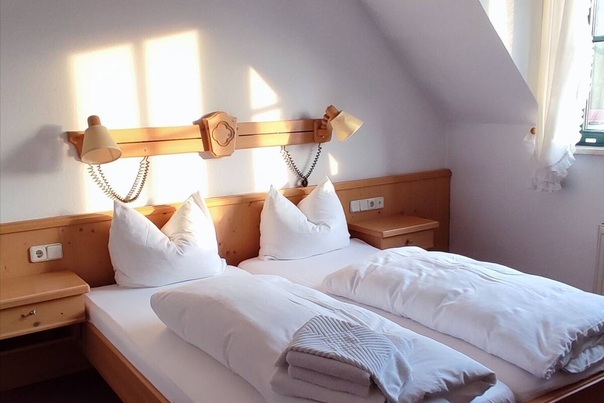 Ein ordentlich bezogenes Bett mit weißen Leinen und Kissen, einem Holz-Kopfteil und Nachttischlampen.