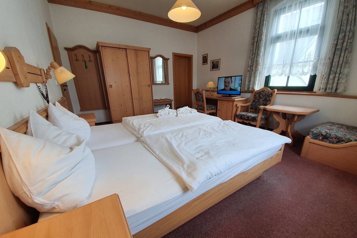 Ein Hotelzimmer mit einem großen Bett, Holzmöbeln, einem Schreibtisch mit Computer und einem Vorhangfenster.
