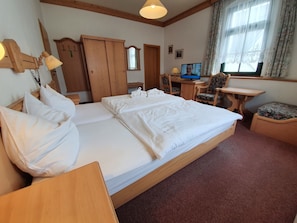 Una habitación de hotel con una cama grande, muebles de madera, un escritorio con una computadora y una ventana con cortinas.