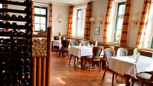 Comedor con varias mesas y sillas, una cava de vinos y vistas al exterior a través de ventanas.