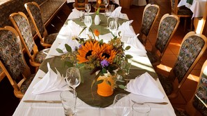 Una larga mesa de comedor dispuesta para una comida, con sillas, un jarrón de flores y copas de vino.
