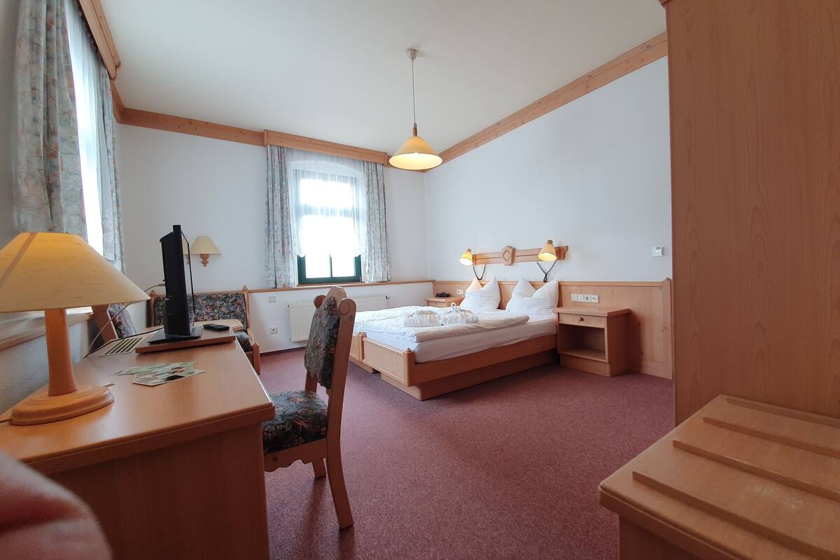 Ein Hotelzimmer mit Bett, Nachttischen, einem Schreibtisch mit Lampe, einem Sessel und einem Fenster mit Vorhängen.