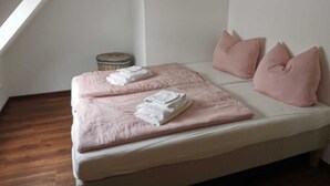 Una cama bien tendida con ropa de cama y almohadas rosadas, una pequeña cesta redonda de mimbre y una pared blanca.