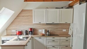 Cocina compacta con armarios blancos, encimera de madera y horno empotrado. Hay una ventana que proporciona luz natural, y el piso es de madera.