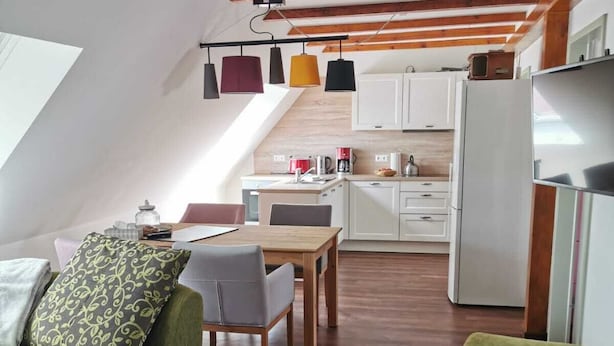 Un apartamento estilo loft con comedor, kitchenette y un sofá verde con cojines estampados.