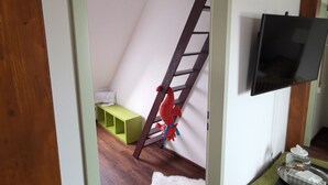 Una habitación con piso de madera, un banco verde, un tapete blanco y esponjoso, un adorno de pez rojo y un televisor montado en la pared.