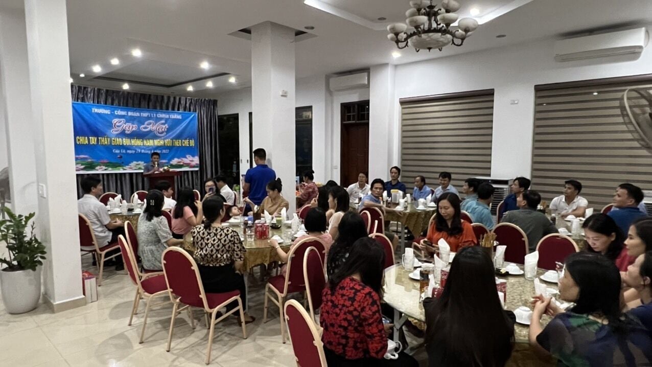 A conference room with round tables and chairs, a stage with a banner, and a chandelier.