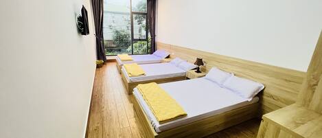 A hotel room with two single beds, wooden flooring, a window with curtains, and a view of greenery outside.