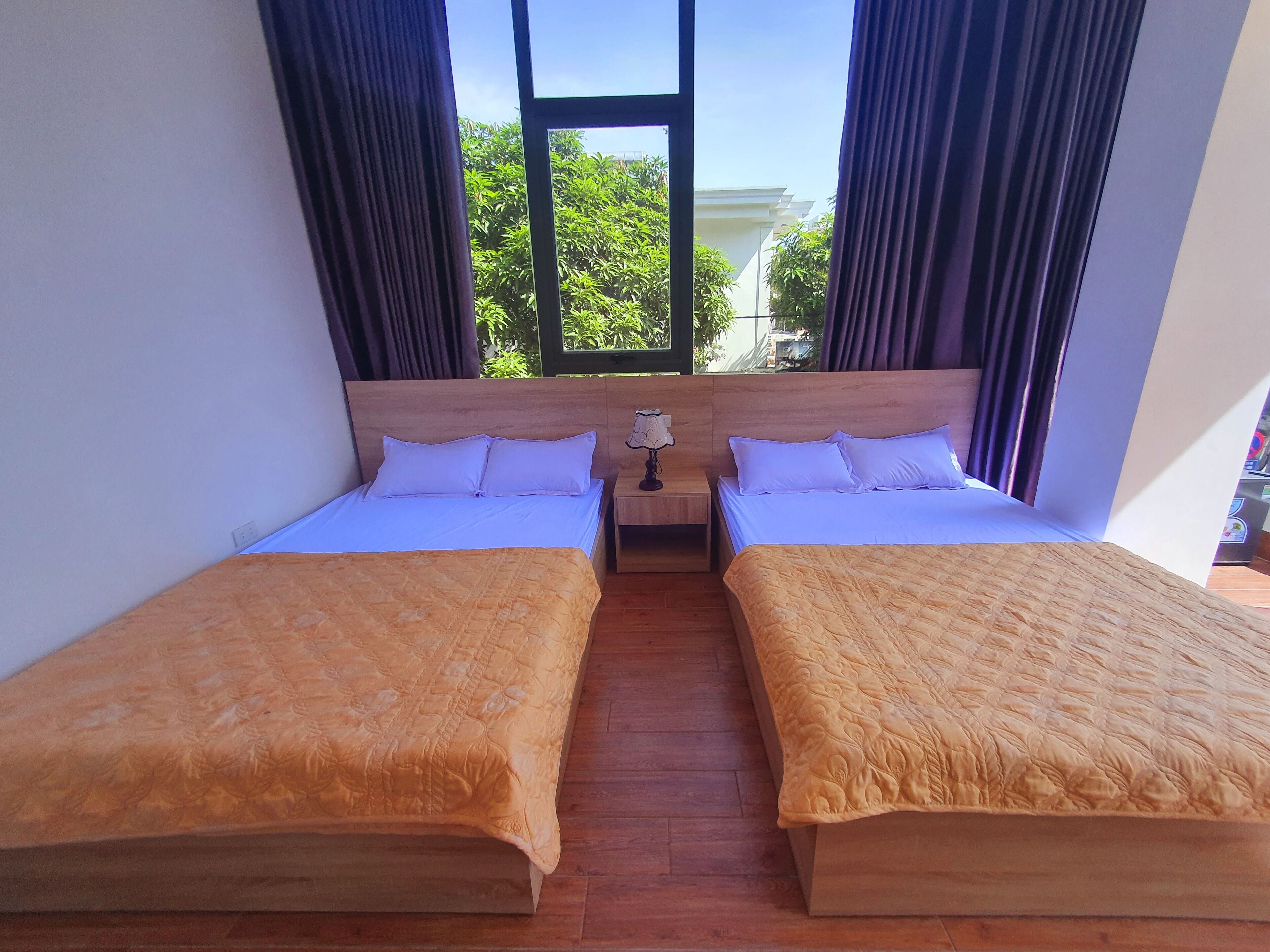 A hotel room with two single beds, a nightstand with a lamp, and a window with curtains.