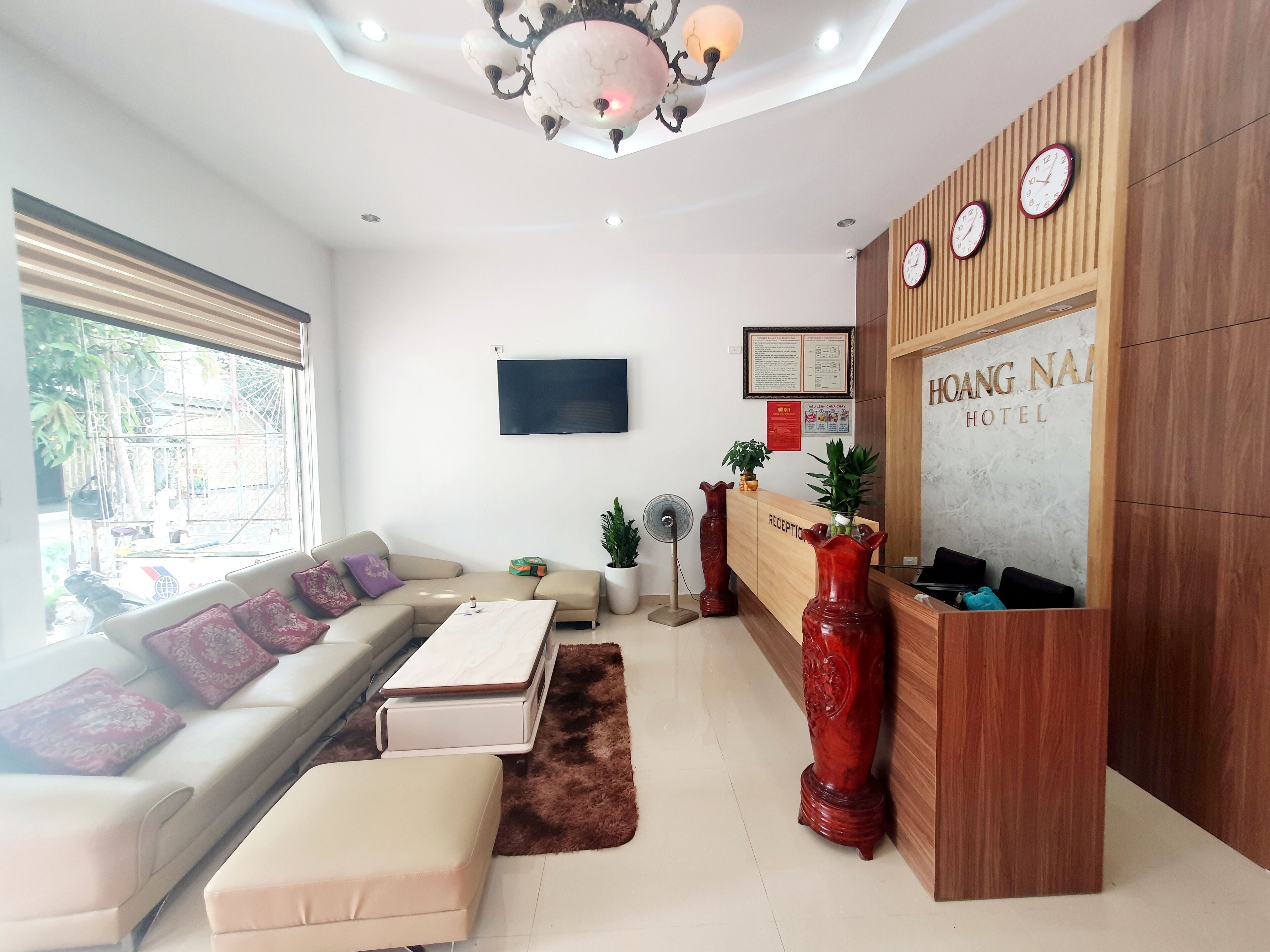 A hotel reception area with a sofa, a reception desk, a TV, and a large window.