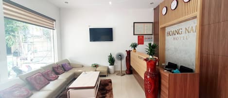 A hotel reception area with a sofa, a reception desk, a TV, and a large window.
