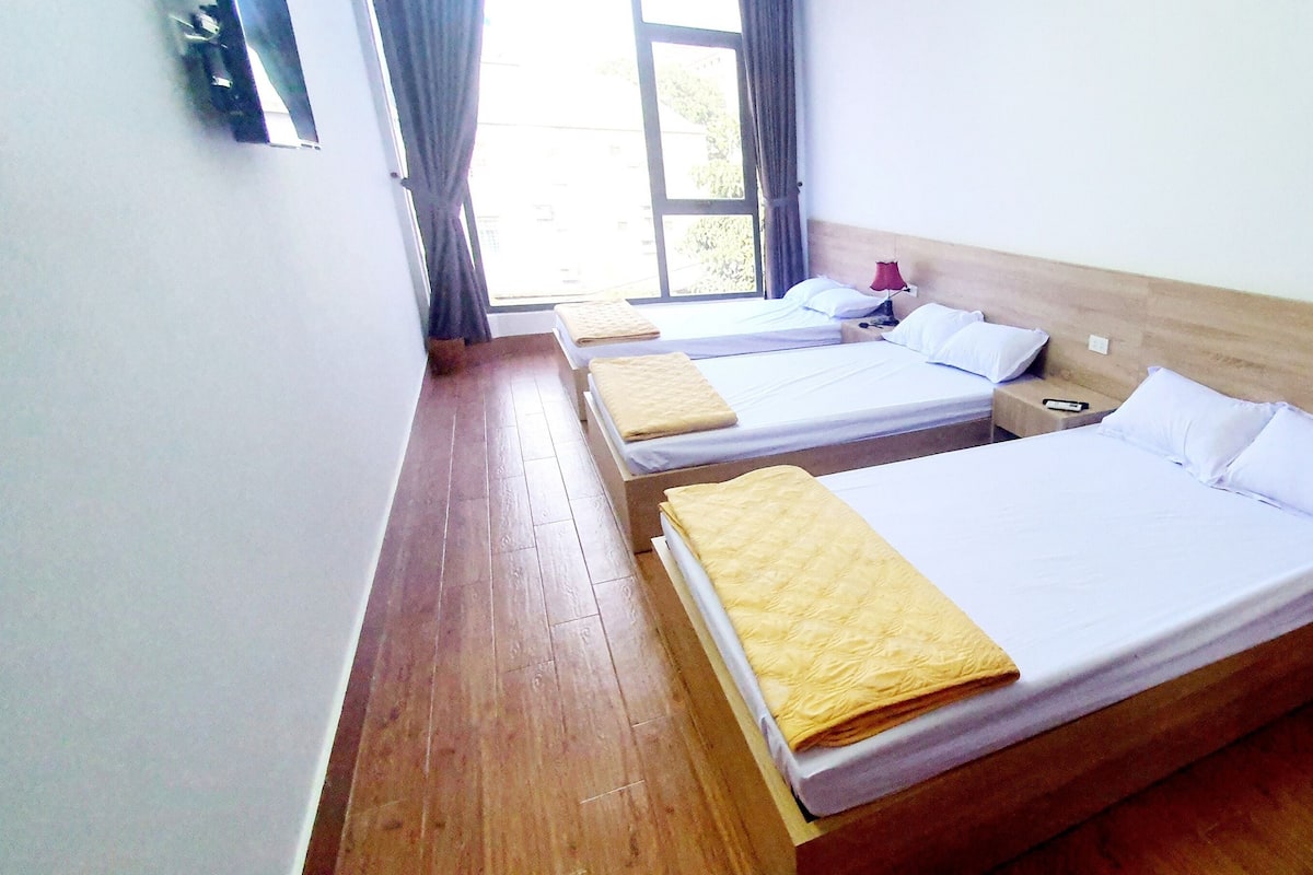 A room with three single beds, wooden flooring, and a window with curtains.