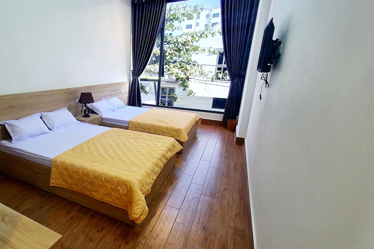 A hotel room with two beds, wooden flooring, a window with curtains, and a wall-mounted TV.