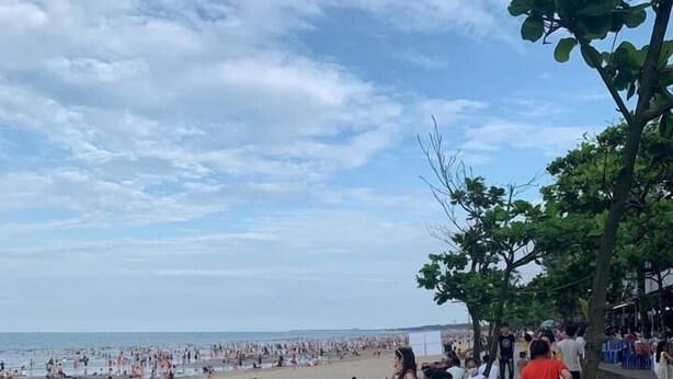 Een strand met mensen, een rij houten stoelen en een betonnen pad.