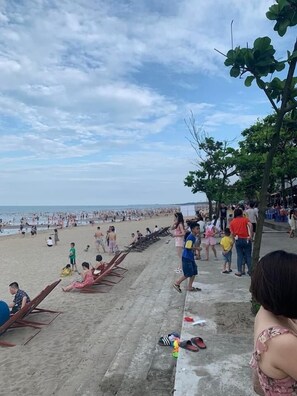 Una playa con gente, una fila de sillas de madera y un camino de hormigón.