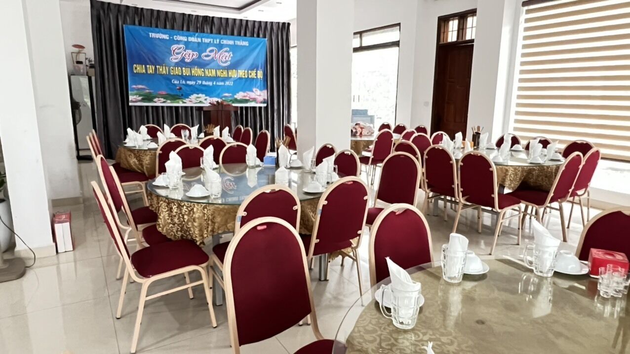 Una sala conferenze con tavoli rotondi e sedie rosse, uno schermo grande e un palco.