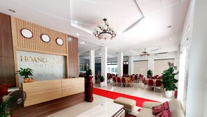 Een hotel receptie met een receptiebalie, een kroonluchter en een zithoek met een rode loper.