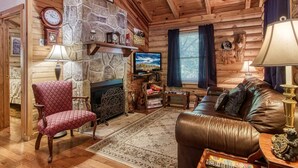Interior acogedor de una cabaña de madera con chimenea de piedra, sofá de cuero y televisor.
