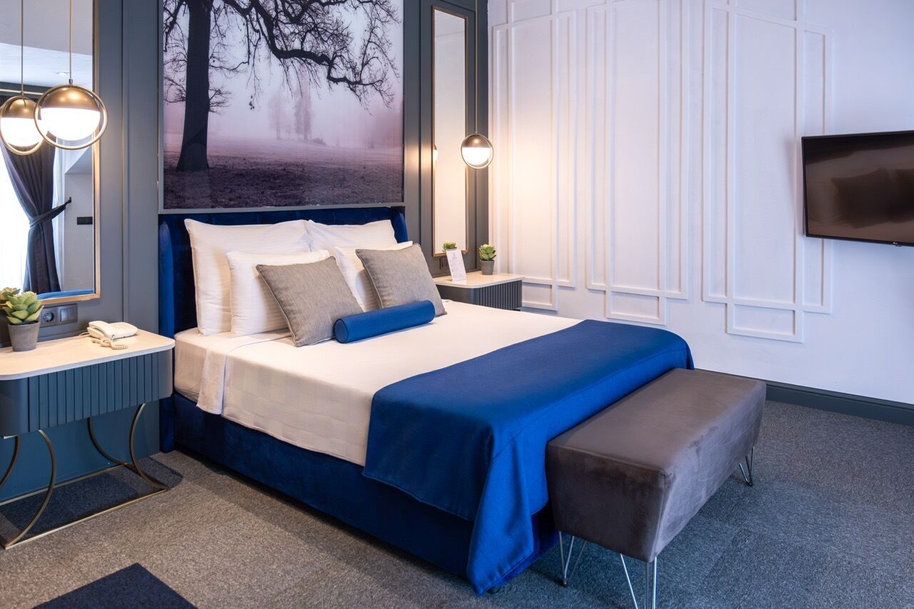A modern hotel room with a large bed, bedside tables, a flat-screen TV, and a large window with a view.