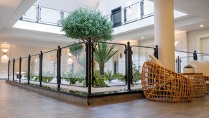 Un hall d’entrée spacieux avec une rambarde en verre, un arbre central et des meubles en osier.