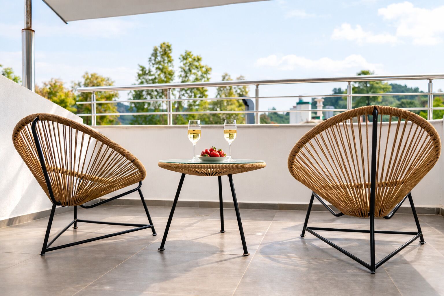 A balcony with two wicker chairs, a small table, and two glasses of white wine.