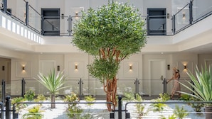 Un vaste atrium intérieur avec un arbre central, de nombreuses portes et une personne qui marche.