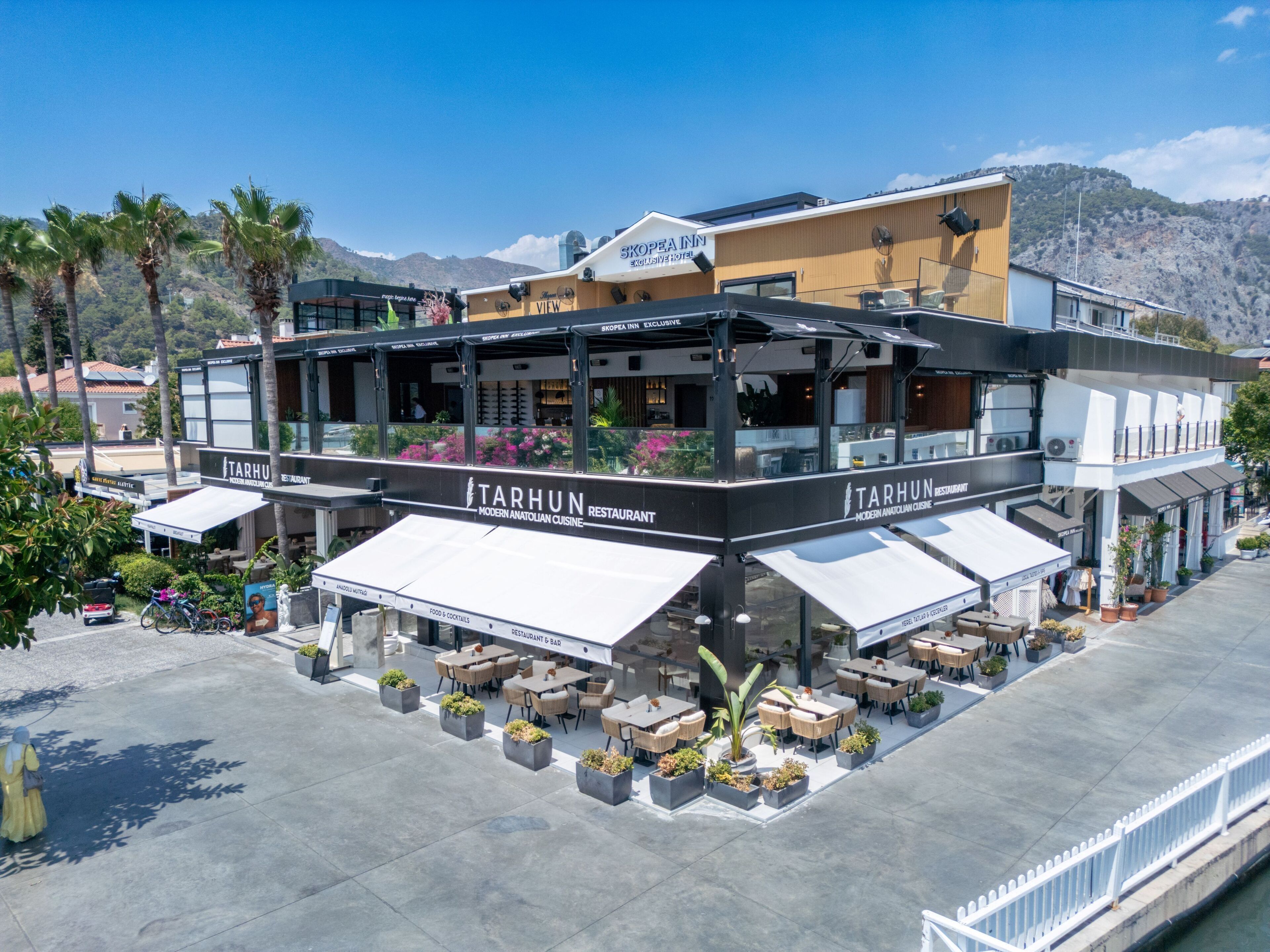 Un ristorante moderno con posti a sedere all'aperto, chiamato 'TARHUN', con una terrazza e vista sulla zona circostante.