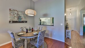 Een eethoek met een ronde tafel, gestreept stoelen, een hanglamp en een spiegel aan de muur.