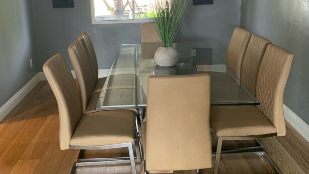 Un coin repas avec une table à plateau de verre entourée de six chaises rembourrées, un vase avec des plantes vertes et deux tableaux accrochés aux murs.