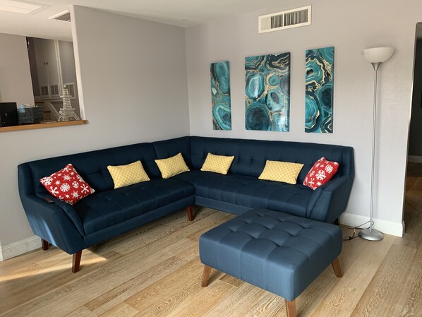 Un salon moderne avec un canapé d’angle bleu foncé, un pouf assorti et trois tableaux abstraits accrochés au mur.