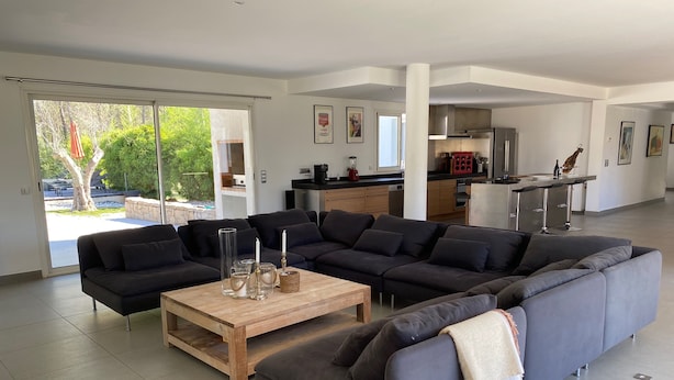 Een moderne woonkamer met een hoekbank, een houten salontafel en een keuken op de achtergrond.