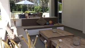 Een terras met een bank, houten tafels en decoratieve planten.