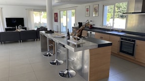 Een moderne keuken met een centraal eiland, roestvrijstalen apparatuur en een eethoek met barstoelen.