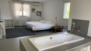 Een moderne slaapkamer met een groot bed, een klein nachtkastje, een stoel, een bureau en een badkamer met een bad en douche.